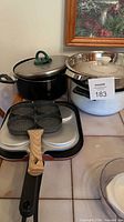 Group showing two lidded pots, metal colander nested, four-cup egg pan and griddle plate