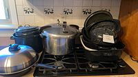 Group shot on stovetop showing pressure cooker, stock pot, stainless lid and stacked enamel roasters