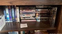 Shelf view showing six clamshell VHS tapes and multiple stacked DVDs with cases