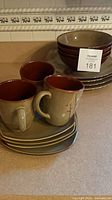 Stacked dinner plates, bowls and mugs displaying exterior olive glaze, interior brown glaze and branch motif