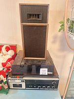 Front view showing integrated stereo unit with turntable dust cover, cassette deck, knobs, and two stacked speakers