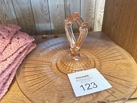 Pink pressed glass serving plate with double ring handle beside folded pink crocheted blanket