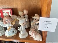 Shelf showing several Precious Moments figurines: angel, graduate, couple, cowboy, rabbit, plaques