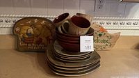 Stack of brown/tan stoneware plates, bowls and mugs showing exterior and interior colors