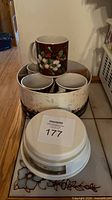 Top view of four burgundy holly mugs nested in decorative sleeve with inverted kitchen scale placed on top