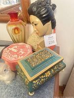 Group showing green floral trinket box, pink jasperware box, amberina pitcher, Asian head wall mask, frosted bird