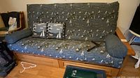 Front view of futon showing wooden frame, nautical upholstery, square and bolster pillows, and drawers