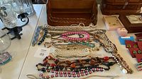 Open wooden jewelry box and spread of various bead, faux pearl and metal costume jewelry pieces on table