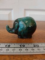Left side view of green/brown drip glaze elephant next to ruler