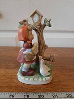 Left side view of ceramic figurine showing girl, basket, geese, tree shrine