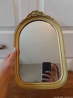 Full view of gold-framed arched mirror held by hand