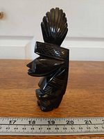 Left profile of entire obsidian warrior showing headdress detail with ruler for scale