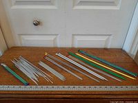 Full assortment of knitting needles laid out on wooden surface with ruler for scale