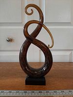 Full frontal view of brown and black twisted glass Treble Clef sculpture on base with ruler for scale