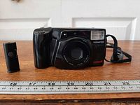 Front view of camera with lens cover closed, built-in flash visible, remote standing beside camera