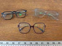 Three pairs of eyeglasses laid out with ruler for scale
