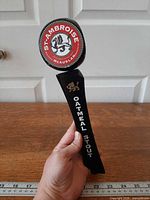 Full view of tap handle front showing logo and lettering with ruler for scale