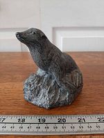 Front left view of soapstone seal on rock base with ruler for scale