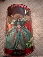 Front view of unopened cylindrical box showing Barbie in green gown