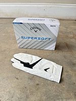 Front view of sealed Callaway Supersoft golf ball box alongside glove
