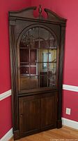 Full front view of corner curio cabinet showing glazed upper door, lower cabinet, crown and finial
