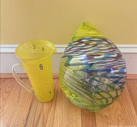 Yellow hand-blown glass pitcher and multicolor teardrop sculpture side by side
