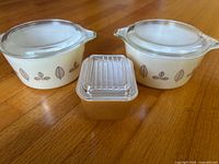 Front view of two leaf-pattern bowls with lids and tan dish with lid