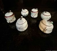 Front view of six porcelain tea canisters on dark surface