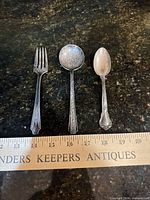 Front view of fork, sugar spoon and teaspoon beside ruler