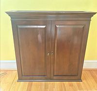Front view of dark cherry veneer cabinet showing two paneled doors and moulded top
