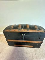 Full front view of dome-top trunk showing wood slats, lock and black painted surface