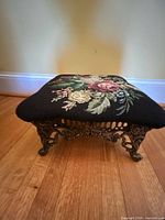 Overall view of footstool front showing needlepoint top and ornate cast iron legs
