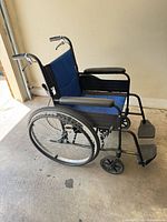 Left side view of folded manual wheelchair showing frame, wheels, footrests