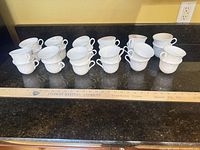 Group of 14 teacups displayed on countertop beside yardstick