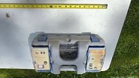 Closed grey Dremel case with blue latches and integrated accessory compartments, tape measure for scale