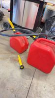 Two red gas cans, yellow spouts and black hose on floor