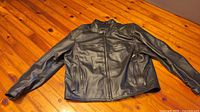 Front view of black leather Harley-Davidson motorcycle jacket laid flat