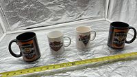 Four Harley-Davidson mugs in a row with measuring tape for scale