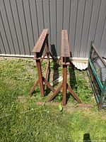 Pair of rusted steel sawhorses with I-beam tops standing on grass