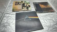 Front view of three Pink Floyd LP sleeves laid out: Dark Side of the Moon prism cover, interior room scene cover, seascape horizon cover
