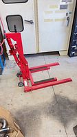 Side view of red hydraulic motorcycle lift showing pump handle, frame, casters