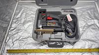 Jigsaw in open grey case with power cord, spare blades in lid, tape measure for scale