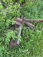 Full view of steel plow attachment lying in grass showing blade and hitch frame