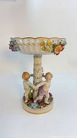 Full view of pedestal compote showing three cherubs and bowl