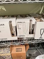 Several sealed IKEA Svalka boxes on shelf with one flute shown
