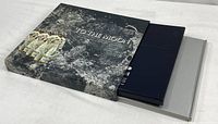 Slipcase with astronaut artwork, navy record binder and grey book partially removed