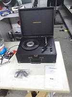 Crosley suitcase turntable open showing platter, tonearm and accessories on table