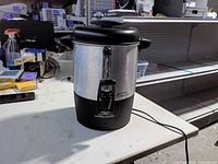 Front view of Hamilton Beach coffee urn showing stainless body, spigot, water level gauge, power indicator light, power cord