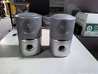 Front view of both silver cylindrical speakers showing grille and bass port