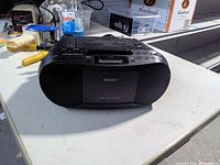 Front view of Sony boombox showing speakers, display, controls and attached power cord
